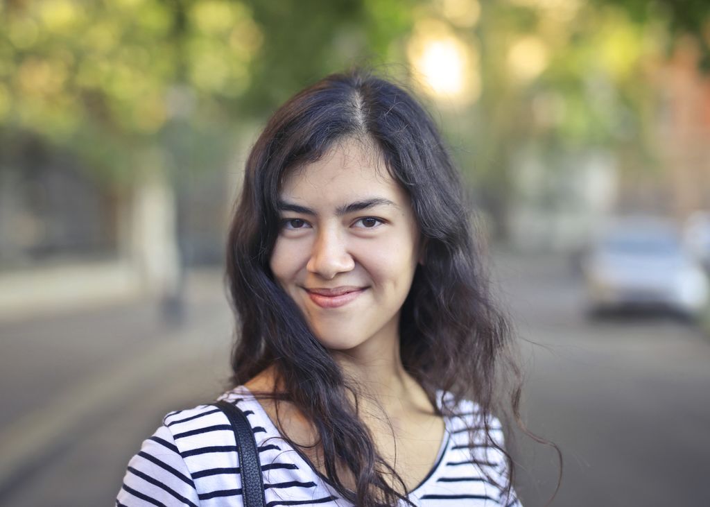 Young woman with brunette hair smiling outdoors on a sunny day.